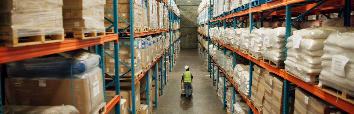 A man in a yellow vest walking down the aisles of a warehouse